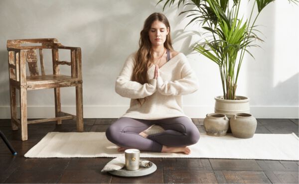 Woman meditating cross-legged in front of a lit candle. A peaceful moment of candle meditation and mindfulness.